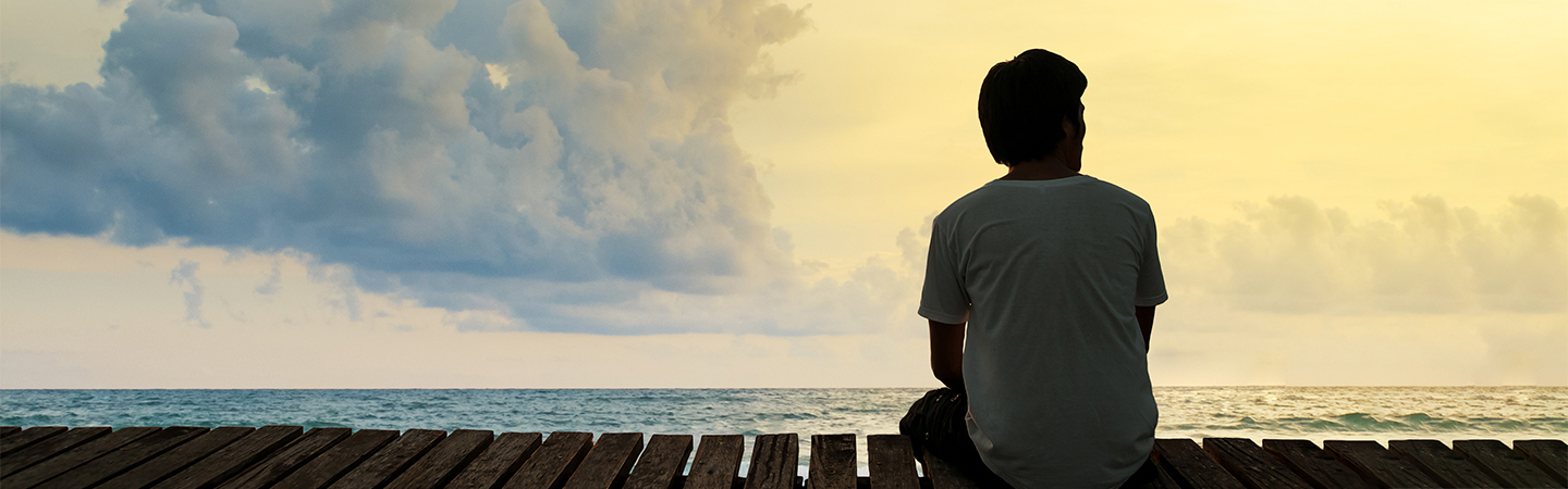 En person sitter på en brygga och tittar ut över havet.