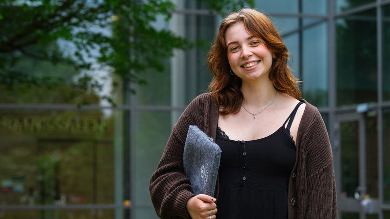 Person står med dator under armen