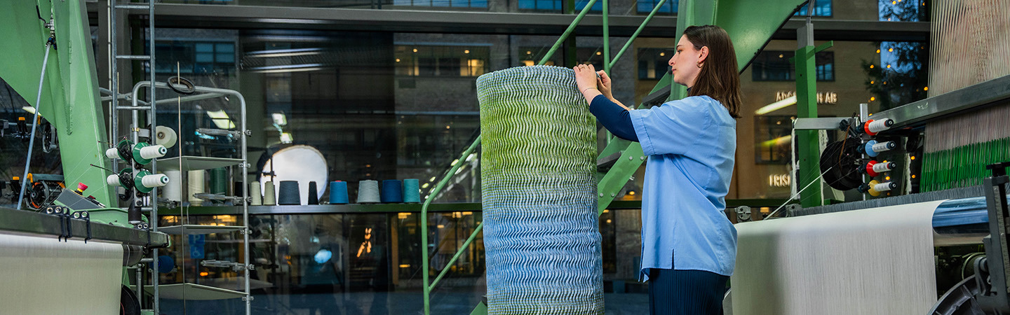 Kvinna utforskar textil i Textilhögskolans vävlabb