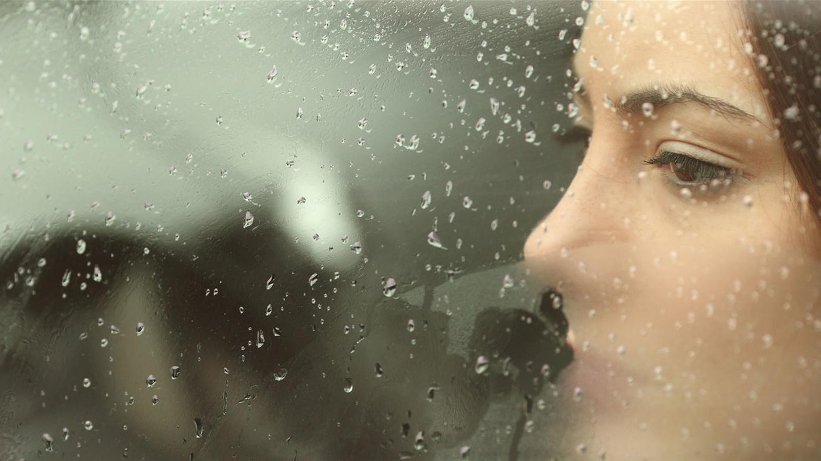 Kvinna ser ut genom bilruta med regndroppar