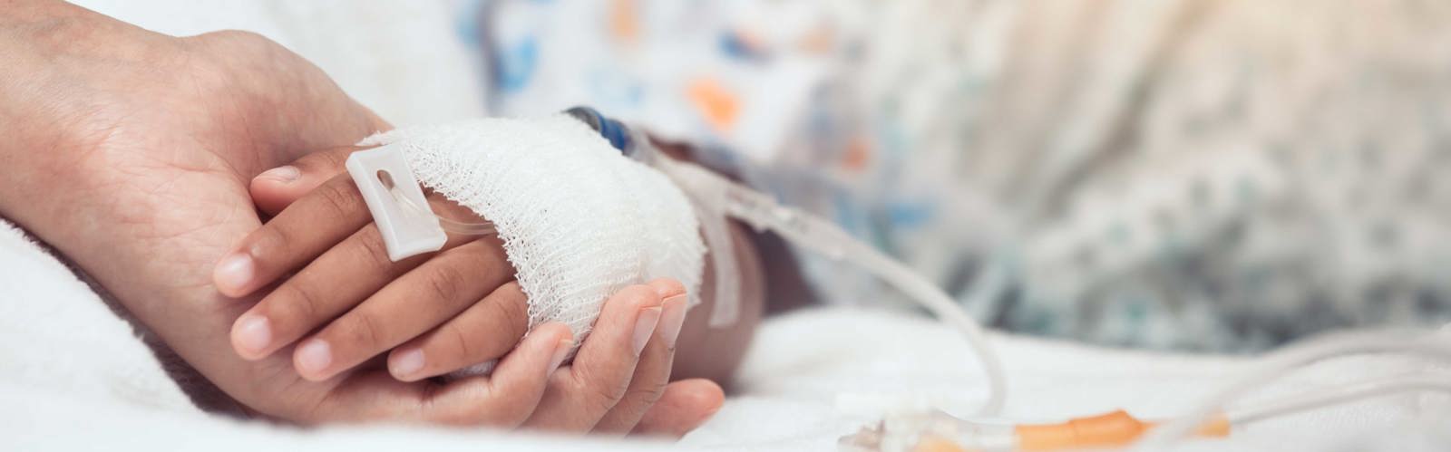 Vuxenhand håller barnhand med dropp på sjukhus