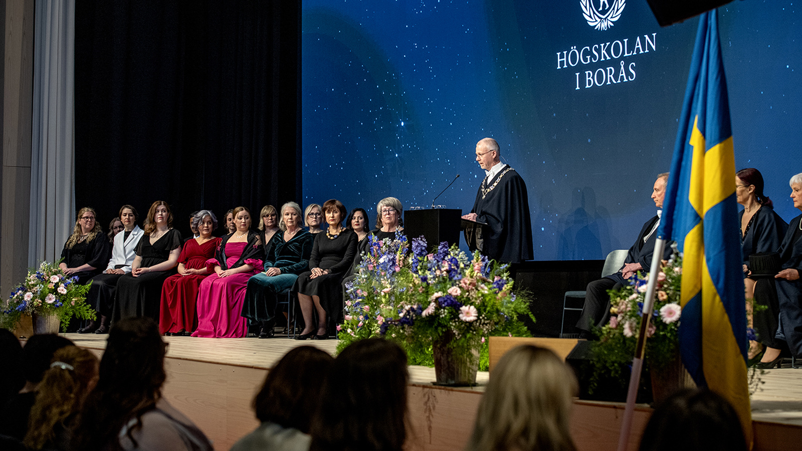 Rektor Mats Tinnsten talar på scen. Till vänster sitter högtidsklädda doktorer.