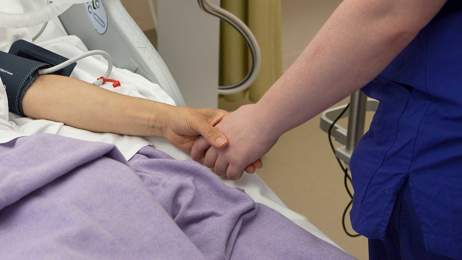 Patient och personal håller hand i intensivvårdsrum