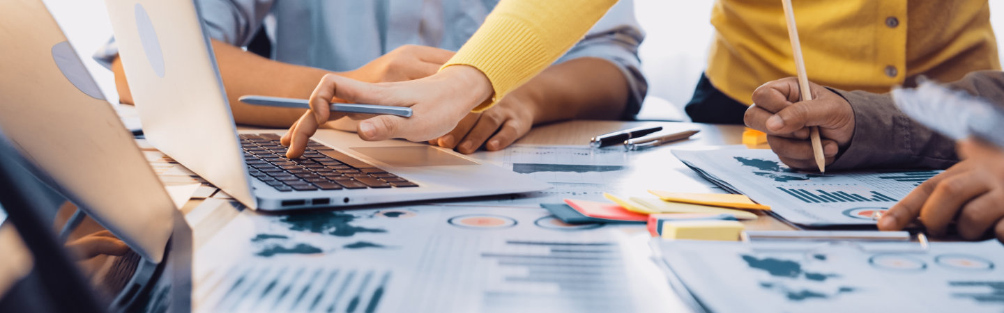 business meeting showcasing professionals collaborating over charts and statistics, utilizing laptops and stationery in a bright, modern office environment