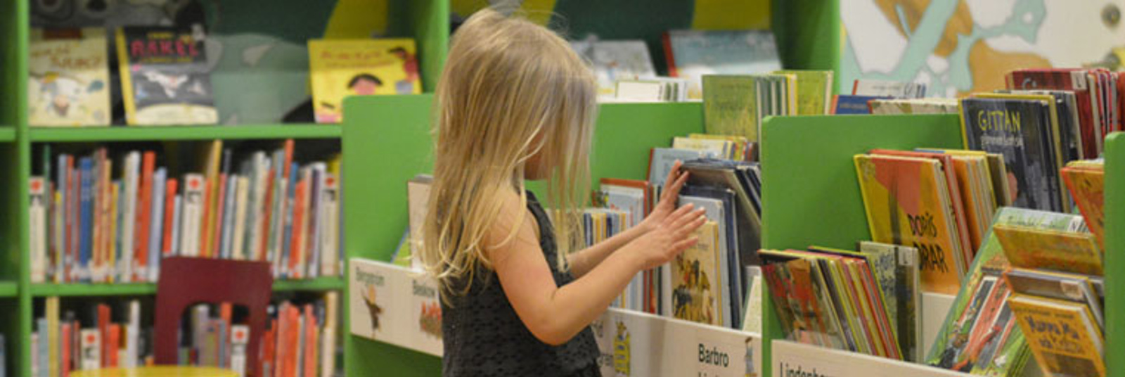 Flicka tittar på barnböcker på bibliotek
